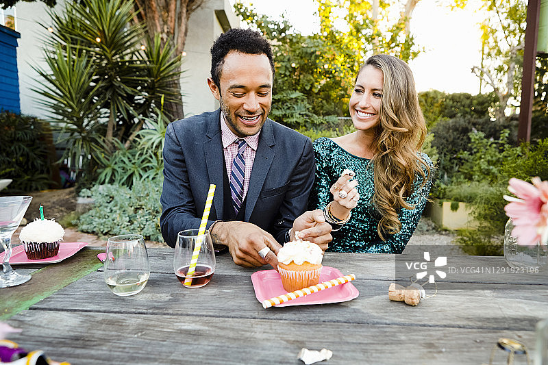 微笑的年轻朋友在花园派对中坐在后院的餐桌旁吃蛋糕图片素材