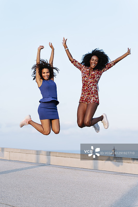 快乐的女性朋友在建筑物屋顶跳跃图片素材