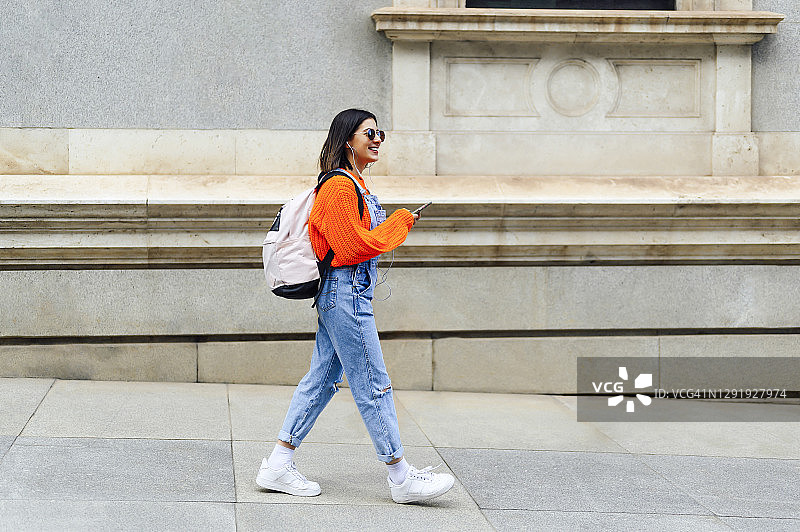 在人行道上行走时使用手机的微笑女性图片素材