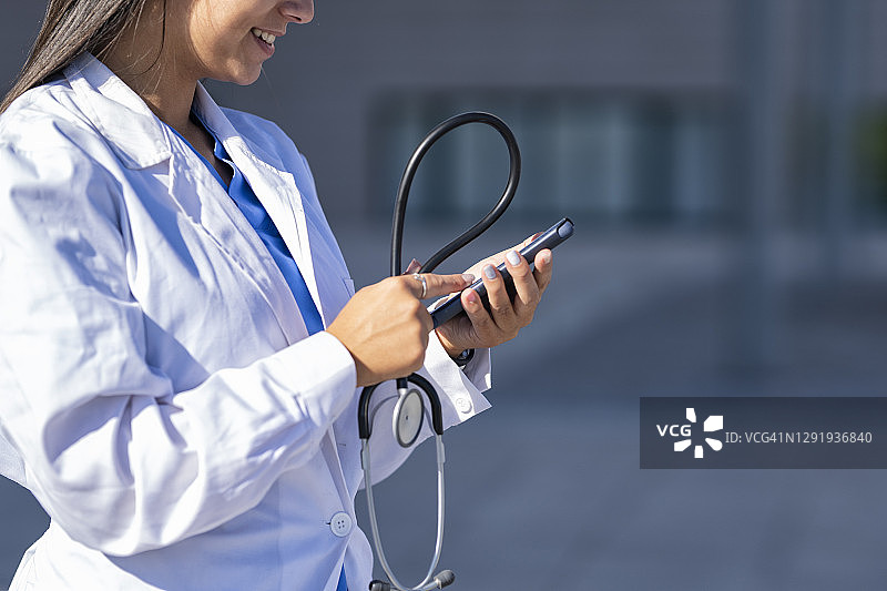 医生使用手机，站在医院背景前图片素材