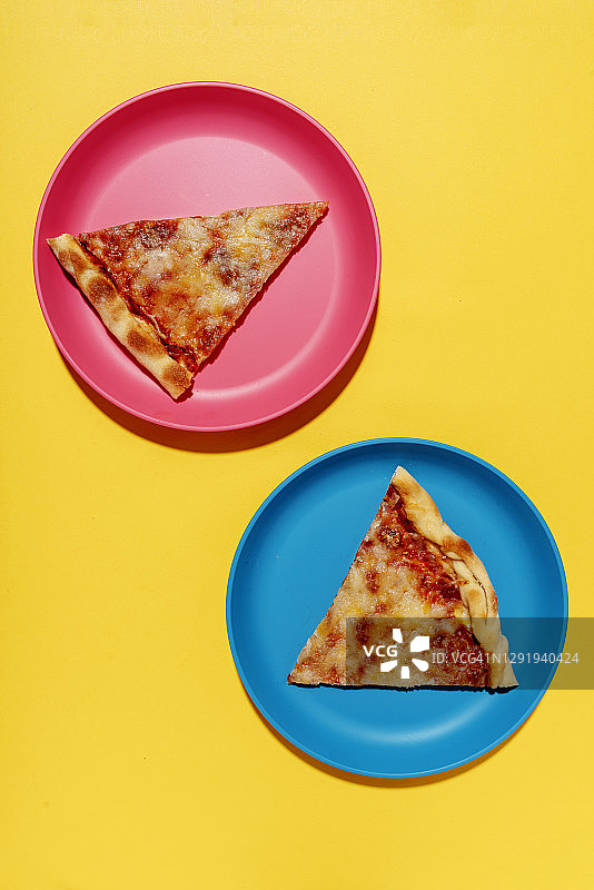 黄色背景下蓝色和粉色盘子上的两片玛格丽特披萨图片素材