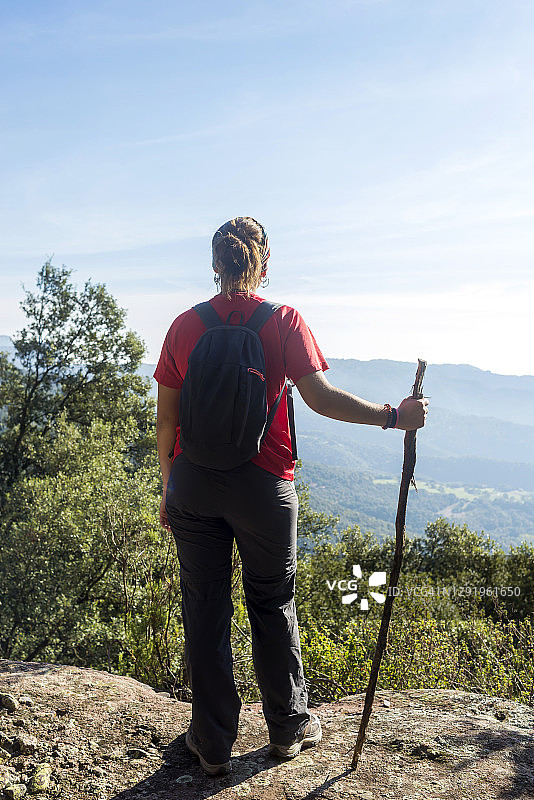 年轻女子站在高山上拄着棍子的背影图片素材
