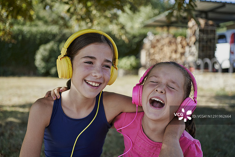 小女孩戴着黄色和粉色耳机在花园里听音乐微笑，幸福的概念图片素材