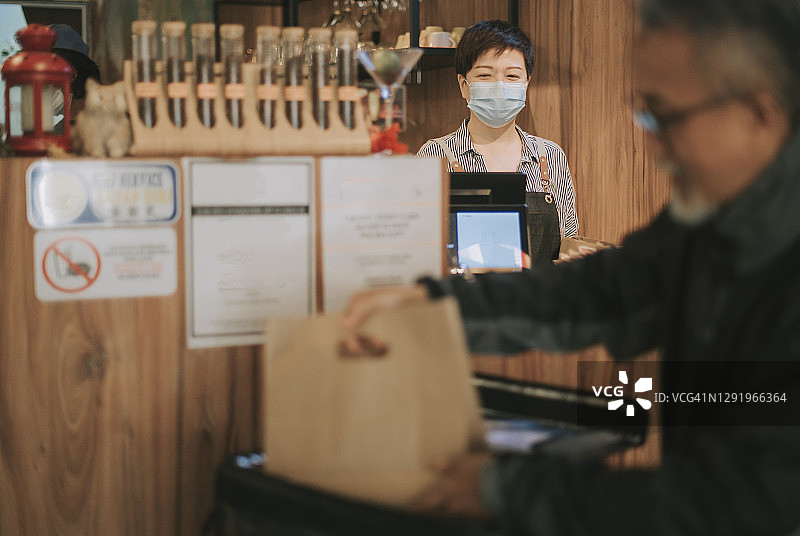 亚洲华人老年男子送外卖，在咖啡馆取餐并放入保温箱图片素材