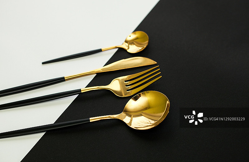 黑白对角线纸背景，黑色和金色餐具平铺。优雅的餐桌布置。图片素材
