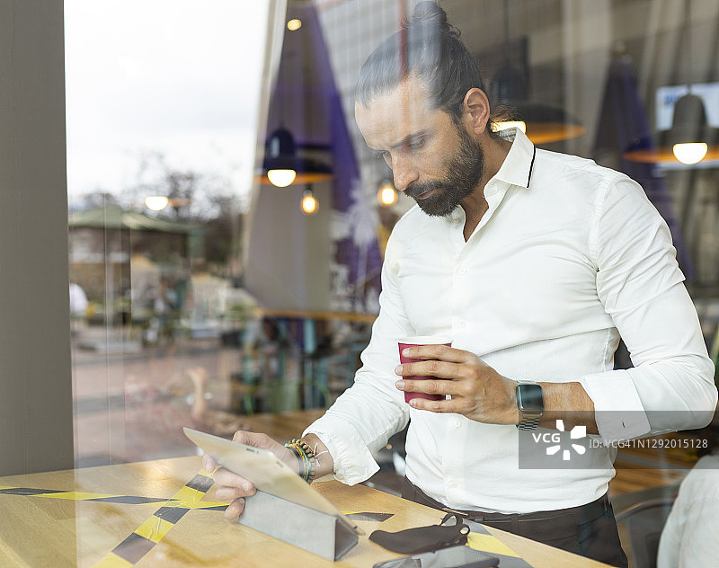 在咖啡馆内，在数字平板电脑前喝咖啡的络腮胡商人抓拍肖像图片素材