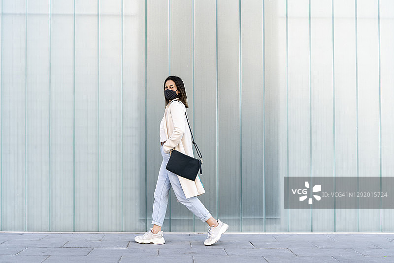 疫情期间，女商人走在玻璃墙旁的人行道上图片素材