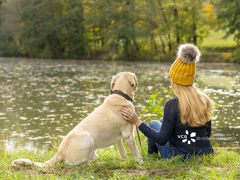秋季，金发女人和狗坐在湖边图片素材
