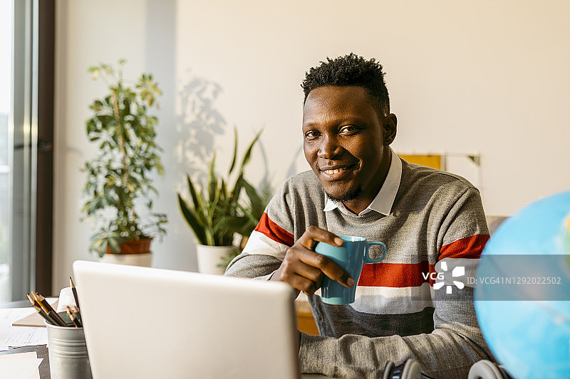 微笑的男企业家在家中办公室里坐着喝咖啡图片素材