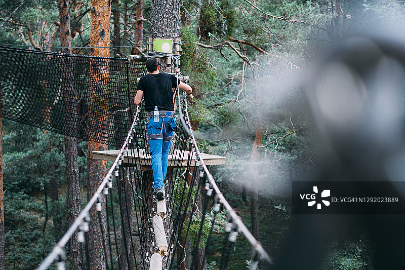 在冒险公园穿越绳索桥的年轻男人图片素材