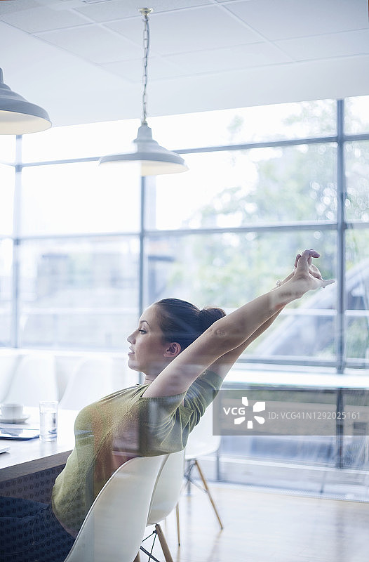 疲惫的年轻女商人坐在办公室的办公桌旁伸展双臂图片素材