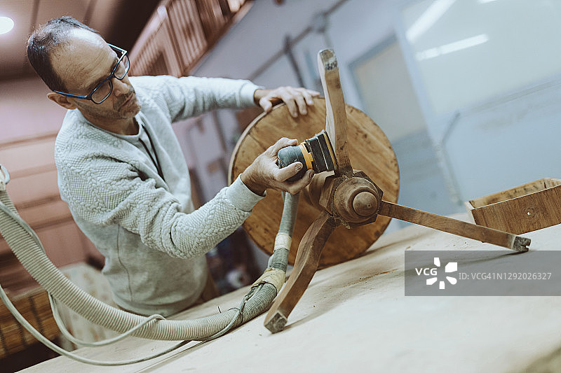 工匠在工作室使用砂光机打磨桌子图片素材