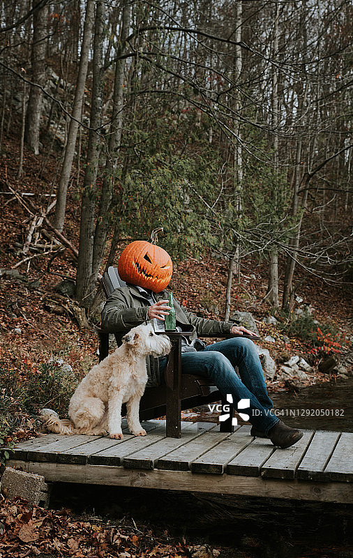万圣节戴着可怕南瓜头，坐在码头上与狗在一起的男人图片素材