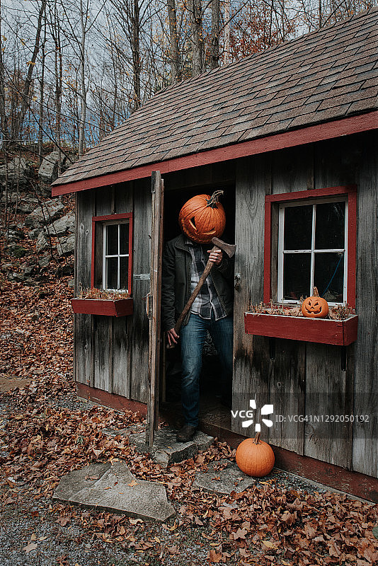 万圣节，戴着可怕的南瓜头，在棚子里拿着斧头的男人图片素材