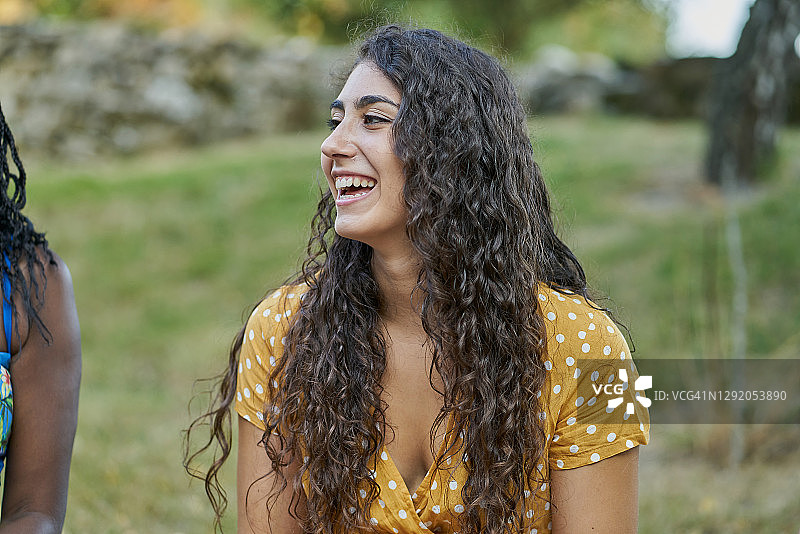 年轻卷发女人在公园里微笑，身穿黄色衬衫图片素材