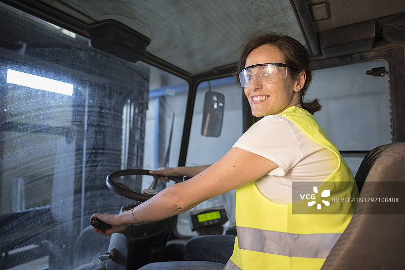 有魅力的成年女性在工业建筑内驾驶大型推土机图片素材