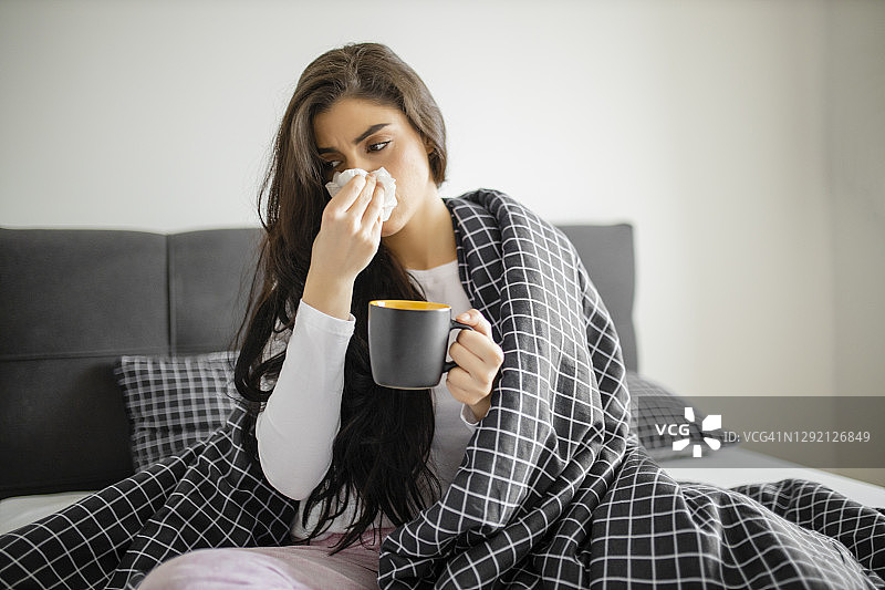 生病发烧的年轻女孩在床上喝茶图片素材