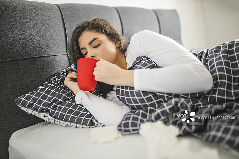 生病发烧的年轻女孩在床上喝茶图片素材