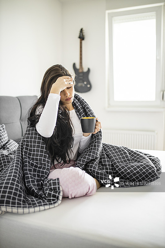 生病发烧的年轻女孩在床上喝茶图片素材