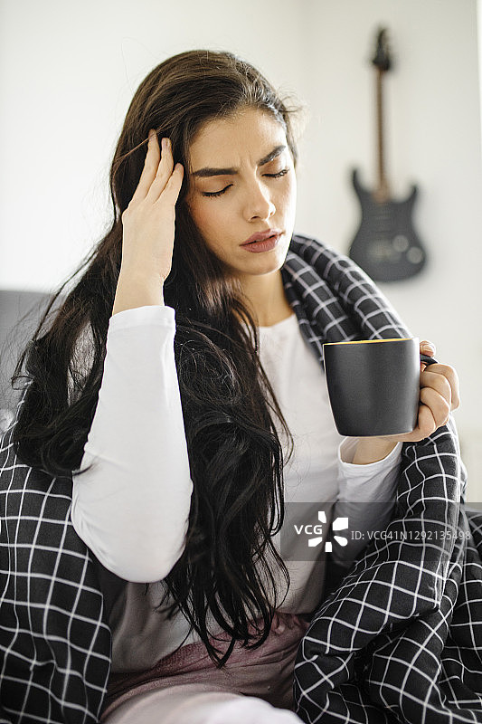 生病发烧的年轻女孩在床上喝茶图片素材