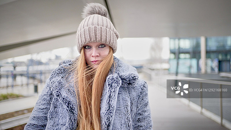 戴着绒球帽和外套看着镜头的红发年轻女子图片素材
