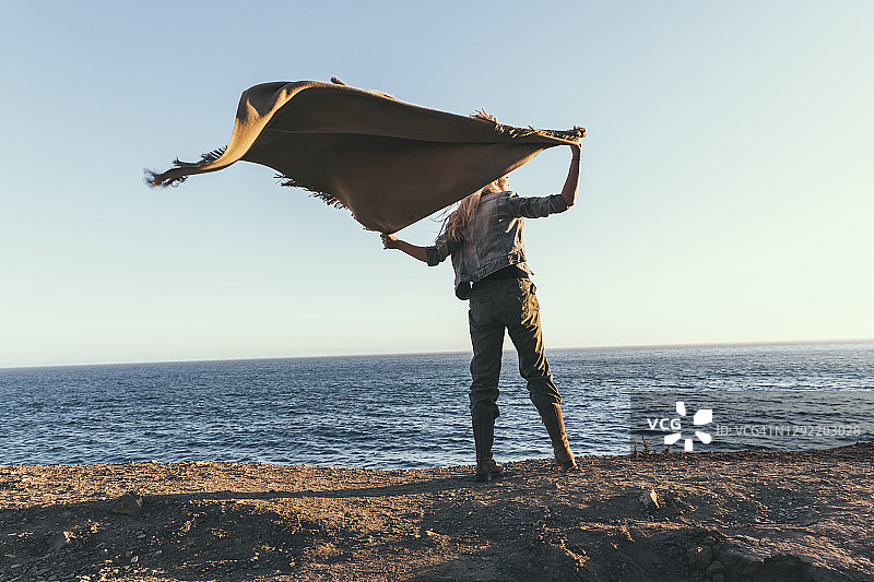 年轻女子在海边拿着毯子的背影图片素材