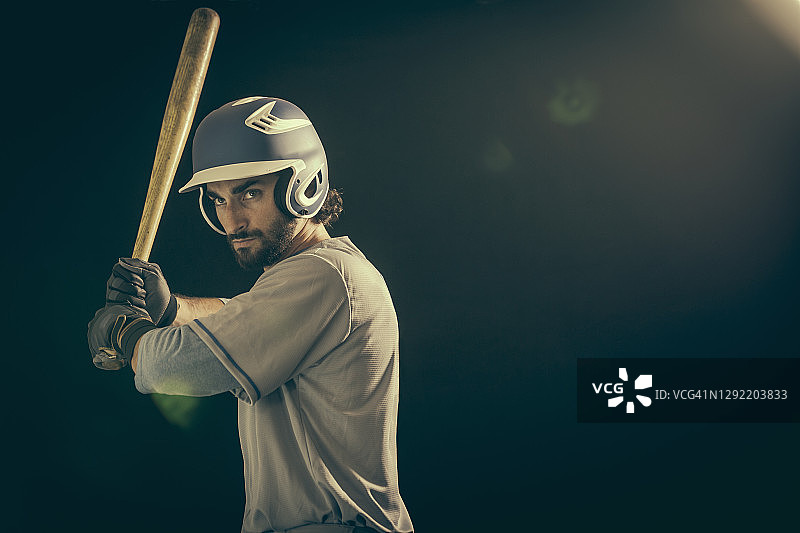 自信的年轻棒球运动员在黑色背景下击球侧视图图片素材