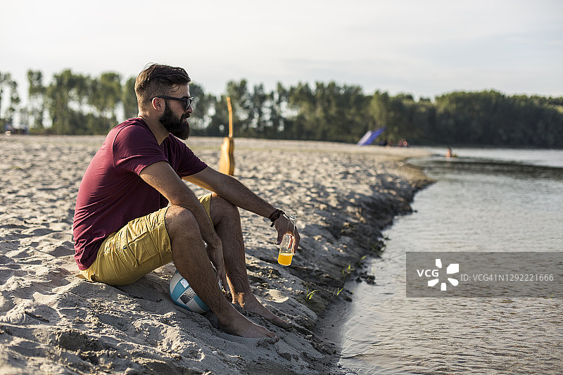 年轻男人坐在河边沙滩享受阳光图片素材