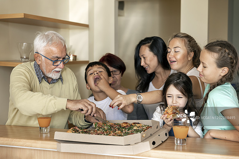 快乐的一家人在厨房里一起吃美味的披萨图片素材