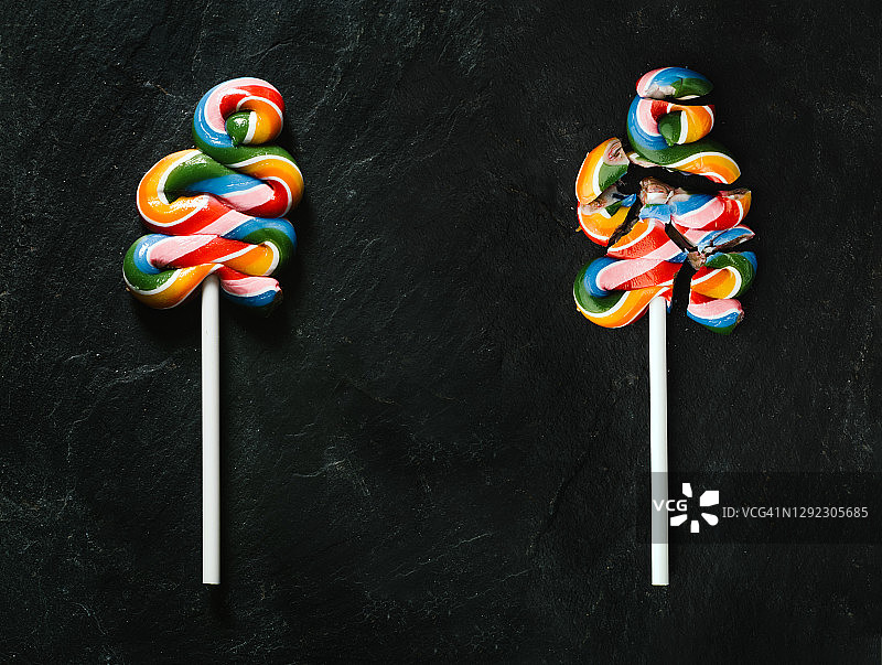 黑色石头背景上的彩色棒棒糖和碎棒棒糖俯视图，停止不健康饮食概念图片素材