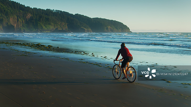 在俄勒冈海滩上骑自行车的男人的无人机航拍图片素材