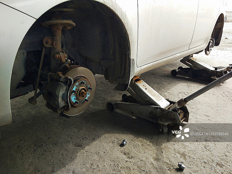 用千斤顶顶起一辆拆掉车轮的旧生锈汽车，更换轮胎、轮胎装配，修复和修复老爷车图片素材