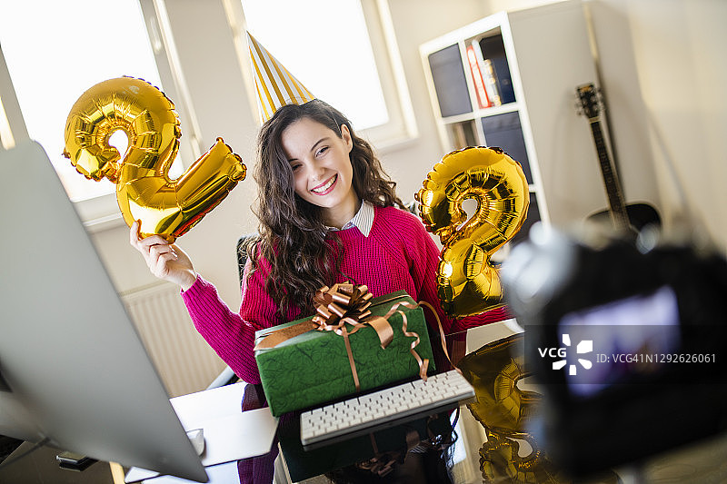女性网红拿着代表即将到来的生日的气球数字22，并为她的视频博客录制教程图片素材
