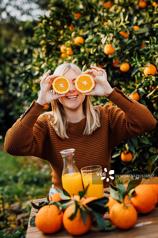 年轻女子拿着自己收获的两个半个橙子，对着镜头微笑图片素材