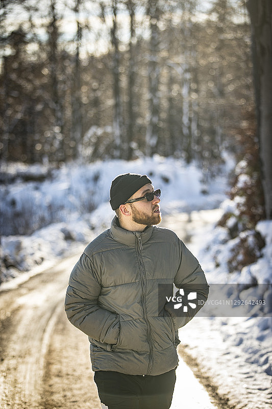 年轻男子在冬季森林的土路上徒步旅行图片素材
