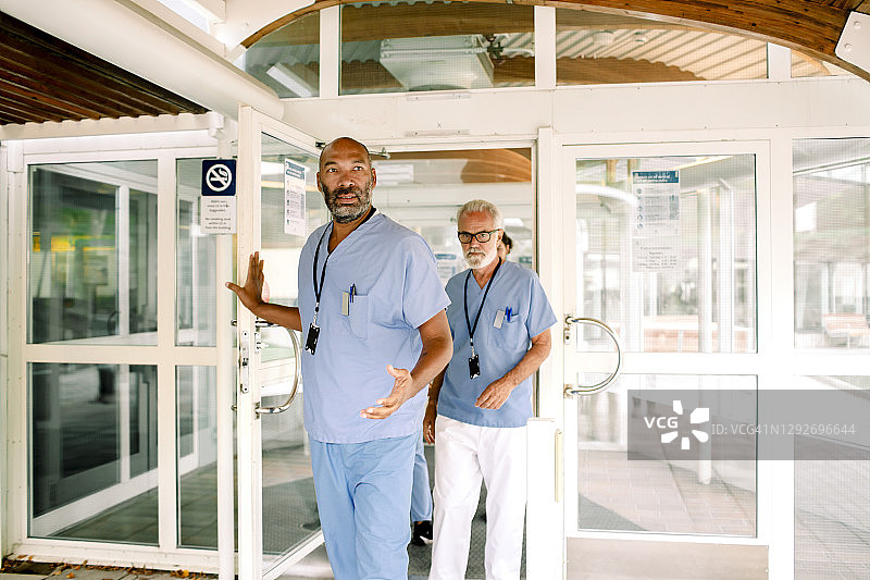 中年护士与资深同事交谈，同时扶着医院的门图片素材