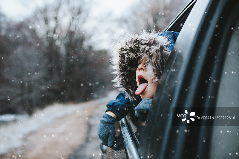 男孩冬季自驾游：从车窗向外看，伸出舌头接雪花图片素材