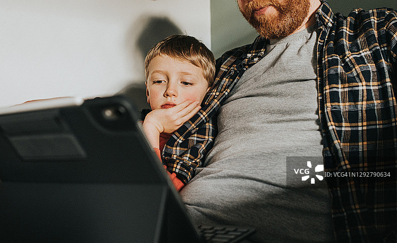 孩子坐在父亲旁边观看电子设备屏幕图片素材