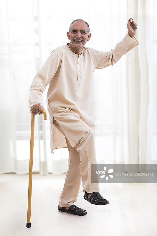 快乐的老年男人拄着拐杖在家里跳舞。（健康和健身）图片素材