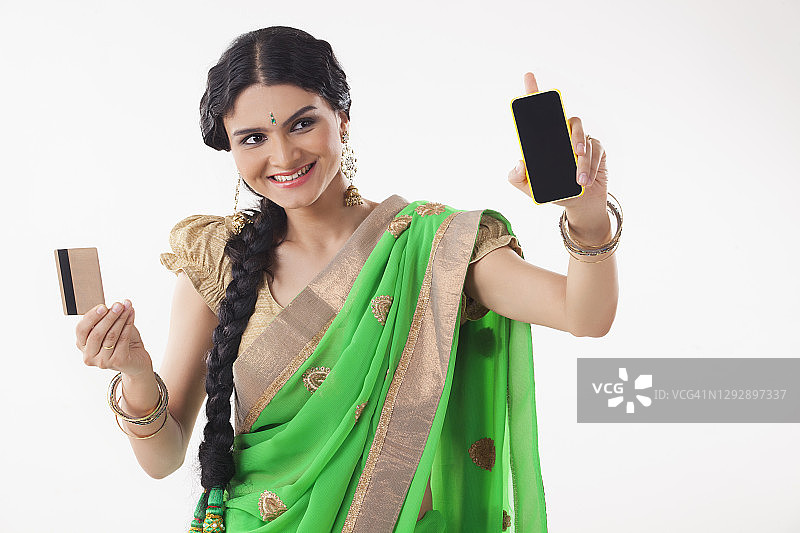 年轻女子微笑，一手拿着手机，一手拿着信用卡（家庭主妇）图片素材