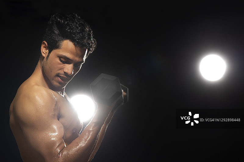 在深色背景下用哑铃锻炼的男人图片素材