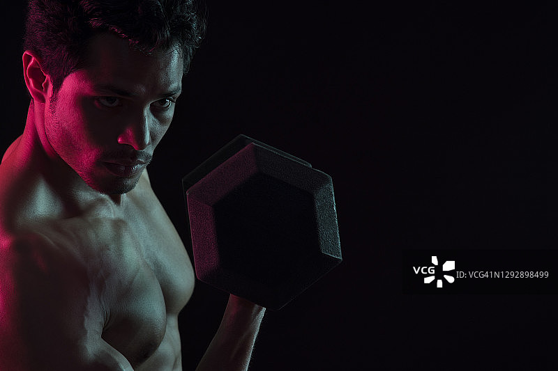 在深色背景下用哑铃锻炼的男人图片素材