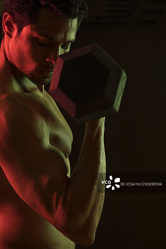 在深色背景下用哑铃锻炼的男人图片素材