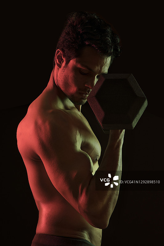 在深色背景下用哑铃锻炼的男人图片素材