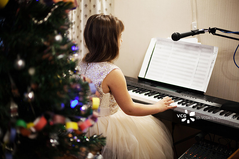 女孩在圣诞树旁弹钢琴图片素材