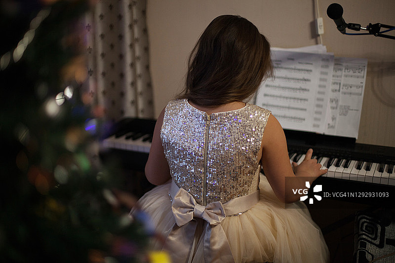 女孩在圣诞树旁弹钢琴图片素材