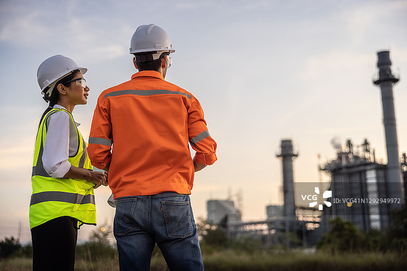 男女工程师在发电厂前一起工作、指点和讨论图片素材