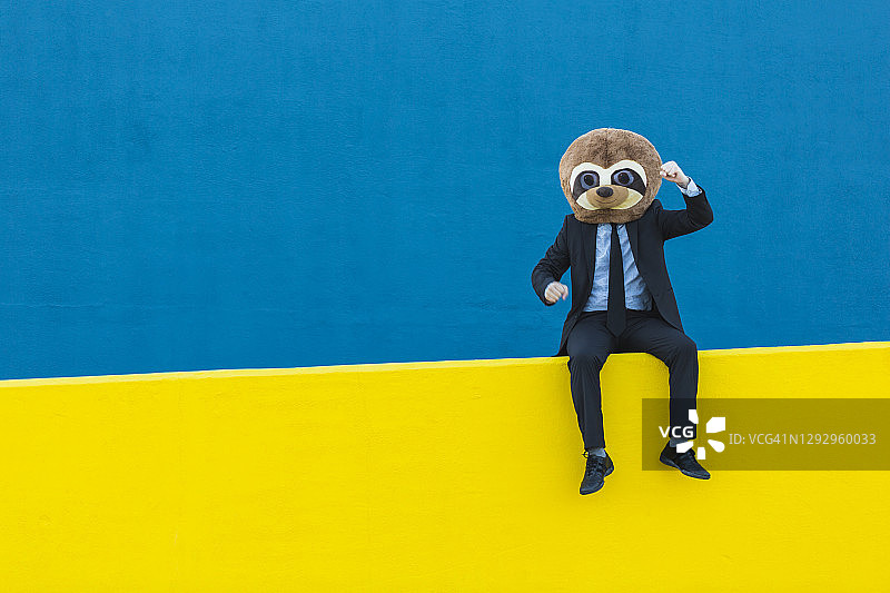 戴狐獴面具的黑西装商人画像，黄色墙面蓝色背景图片素材
