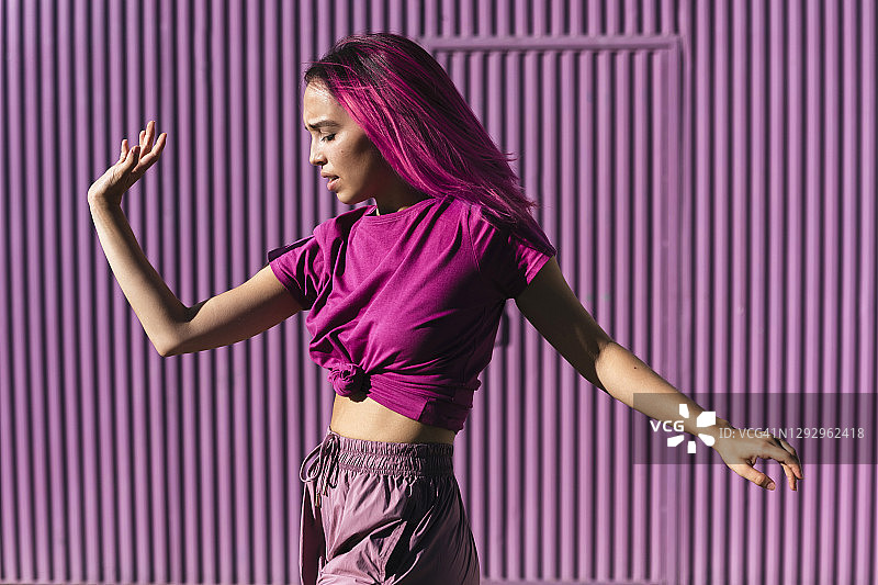 染红发的年轻女人在城市紫色墙壁前跳舞图片素材