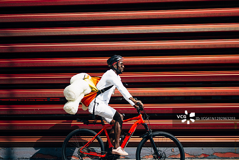 自行车快递员运送泰迪熊经过红墙图片素材